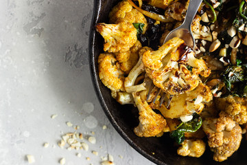 Roasted cauliflower with spinach, raisin and nuts in a cast-iron pan. Light grey background. Copy...