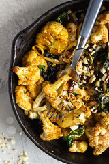 Roasted cauliflower with spinach, raisin and nuts in a cast-iron pan. Light grey background. Copy space. Healthy vegan food.