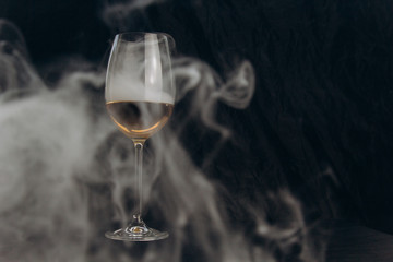 a glass of white wine on a black background. the smoke from the hookah envelops the glass. rest, holiday. alcoholic drink closeup. white fog in a glass. fog