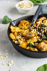 Roasted cauliflower with spinach, raisin and nuts in a cast-iron pan. Light grey background. Copy space. Healthy vegan food.