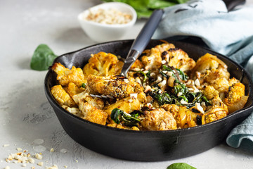 Roasted cauliflower with spinach, raisin and nuts in a cast-iron pan. Light grey background. Copy...