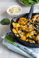 Roasted cauliflower with spinach, raisin and nuts in a cast-iron pan. Light grey background. Copy space. Healthy vegan food.