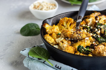 Roasted cauliflower with spinach, raisin and nuts in a cast-iron pan. Light grey background. Copy space. Healthy vegan food.