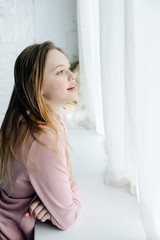 Naklejka premium Teenage kid in pink hoodie standing near window sill