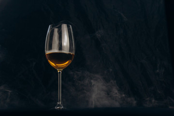 a glass of white wine on a black background. the smoke from the hookah envelops the glass. rest, holiday. alcoholic drink closeup. white fog