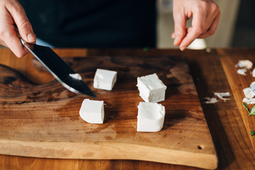 Female chef cutting white cheese on a wooden board