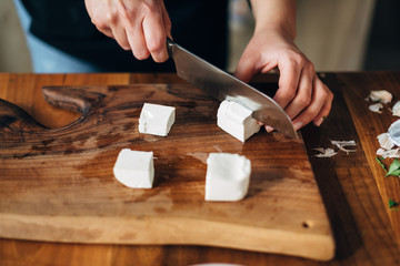 Female chef cutting white cheese on a wooden board