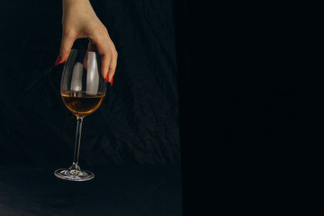 Naklejka na ściany i meble cropped female hand holding a glass of white wine on a black background. rest, holiday, party. isolated alcoholic drink closeup.