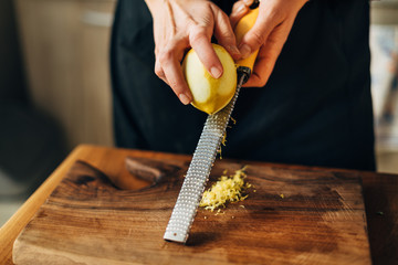 Female chef grating lemon zest on a wooden board - obrazy, fototapety, plakaty