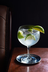 Cold Gin and Tonic or Vodka and Tonic with Ice and Limes in Dark Luxurious Bar with Black Background