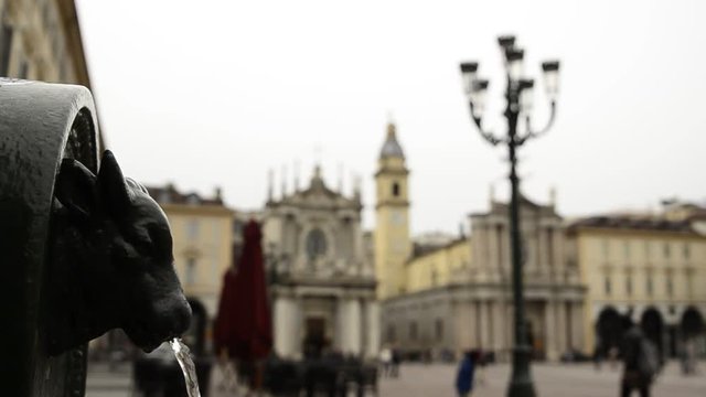 Turin, Piedmont, Italy. April 2019. A look at Piazza San Carlo. On the left in the foreground the fountain with the green bull, called turet, on the right the two twin churches. People are walking.