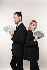 Two employees handsome man and beautiful blonde woman in black suits standing back to back with money in hands