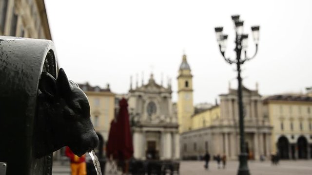 Turin, Piedmont, Italy. April 2019. A look at Piazza San Carlo. On the left in the foreground the fountain with the green bull, called turet, on the right the two twin churches. People are walking.