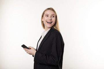 Portrait of impressed amazed attractive fair-haired woman in black suit, holding smartphone and gesturing from excitement