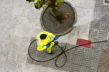 Top view of a Worker cleaning the street sidewalk with high pressure water jet on rainy day