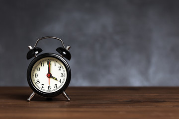 Vintage / retro black analog alarm clock on wooden table with copy space on dark background. Clock hand at 4 o'clock alarm at 6 o'clock