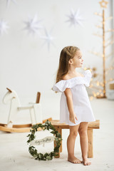 A beautiful little girl sitting on a wooden stool in a beautiful dress in the white room