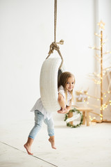 A beautiful little girl playing with a swing boat in the white room