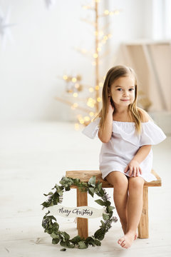 A beautiful little girl sitting on a wooden stool in a beautiful dress in the white room