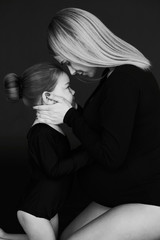 A portrait of beautiful pregnant mother with her little daughterirl dressed in black tights against dark background.