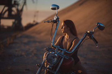 Red-haired woman in sexy lingerie in high heels sits on a motorcycle. Attractive red-haired girl sits on a motorcycle at sunset