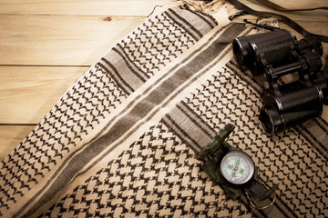 binocular and compass with shemagh scarf on wooden table. travel equipment. copy space. retro style.