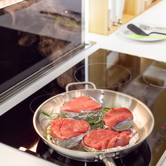 Preparation of steak with rosemary and butter in the skillet on the stove in a light kitchen