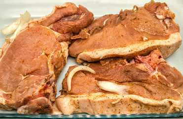 Raw pickled large slices of pork in a clear glass dish seasoned with spices ready for barbecue