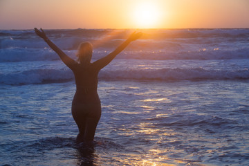 Fototapeta na wymiar Girl at sunset rejoices sea on the beach