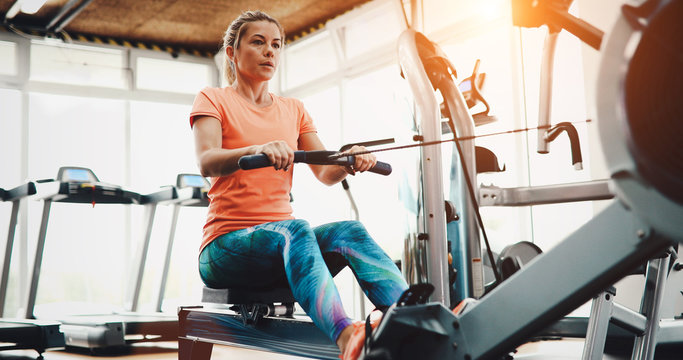 Woman pulling on row machine in fitness - Powered by Adobe