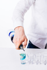 Bartender pours alcoholic drink into small glasses on bar. Colorful cocktails at the bar.