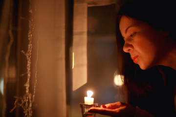Christmas evening girl / beautiful young adult model, dreams and makes wishes at the candles in the New Year's Eve
