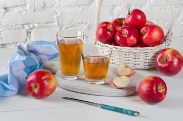 Red apples and juice in glasses and blue napkin on  white table.