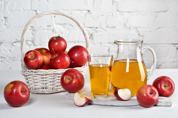 Red apples and apple juice in carafe and glass on white table.