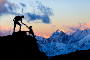 Teamwork concept, couple helping in sunset mountains, silhouette