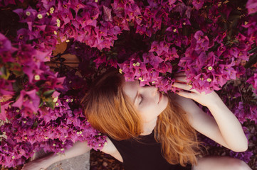 Naklejka premium Portrait of girl with closed eyesamong purple bougainvillaea