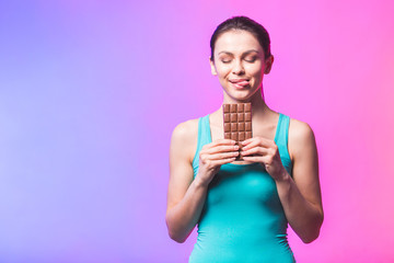 Happy young fitness beautiful lady eating chocolate and smiling. Girl tasting sweet chocolate. Young woman with natural make up having fun and eating chocolate isolated against white background.