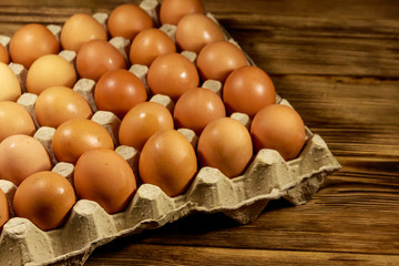 Raw chicken eggs in cardboard pack on wooden table