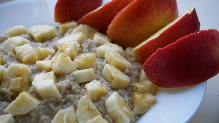 OATED POTENTA IN A PLATE WITH APPLES SALES AND A BANANA WHITE BACKGROUND