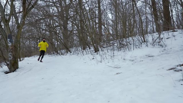 handheld shot of bearded fit man running down the hill in winter forest