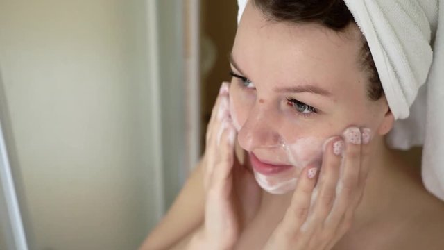 Woman cleaning washing her face with foam in bathroom.