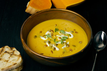 Pumpkin soup in a bowl with cream and pumpkin seeds. Vegan soup. Dark wooden background.