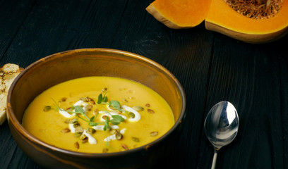 Pumpkin soup in a bowl with cream and pumpkin seeds. Vegan soup. Dark wooden background.