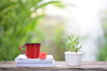 Red cup with flower and notebook on wooden table at outdoor