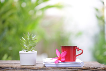 Red cup with flower and notebook on wooden table at outdoor