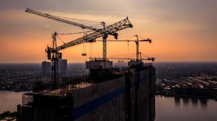Fototapeta premium Construction site silhouette background, Hoisting cranes and new multi-storey buildings, Aerial view Industrial background.