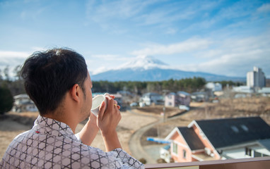Fototapeta premium Young asian man stand looking Mount Fuji on the morning with coffee