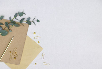 Golden pencil, paper clips, pins, note, envelope, eucalyptus branch on the white texture