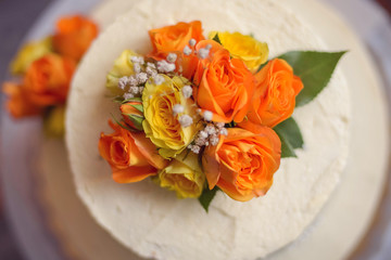 Beautiful delicious wedding cake with white cream, decorated with fresh yellow, white and orange flowers. Top view close-up.
