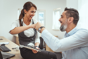 Young successful architect colleagues celebrating successful new project with fist bump in the office.